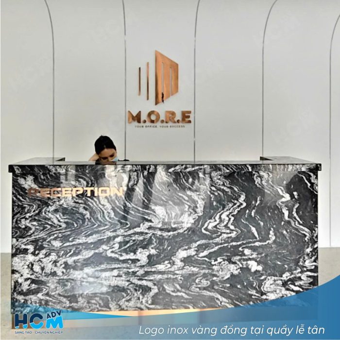 Logo inox quầy lễ tân công ty thiết kế nội thất mạ vàng gắn trên nền đá.